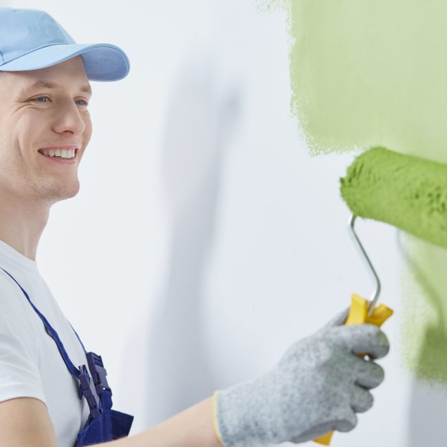 Happy professional interior construction worker painting the wall